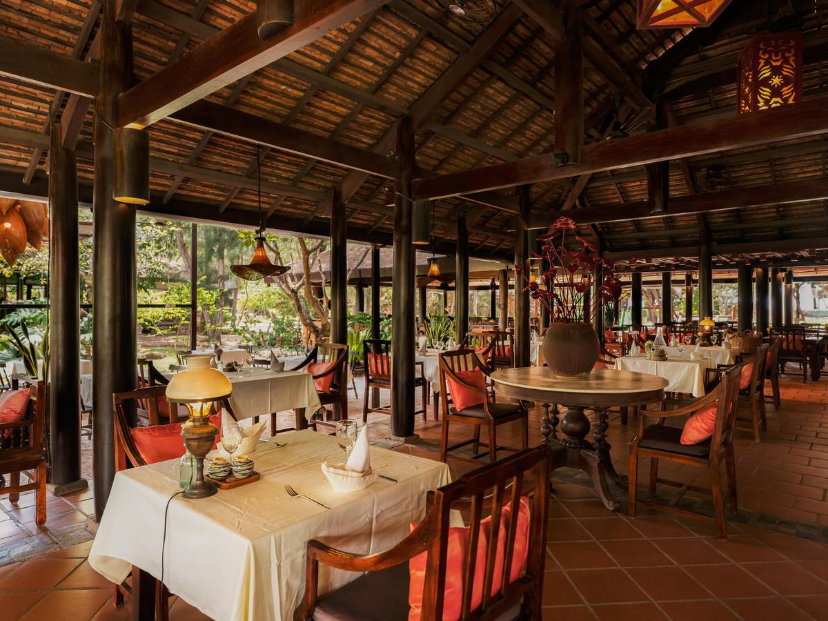 Open-sided restaurant hall with dark timber posts, tiled roof, tables set with white cloths and garden views on both sides