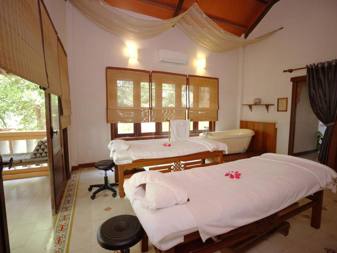 Treatment room with two massage beds, white linen, wooden furniture and bamboo blinds over the windows