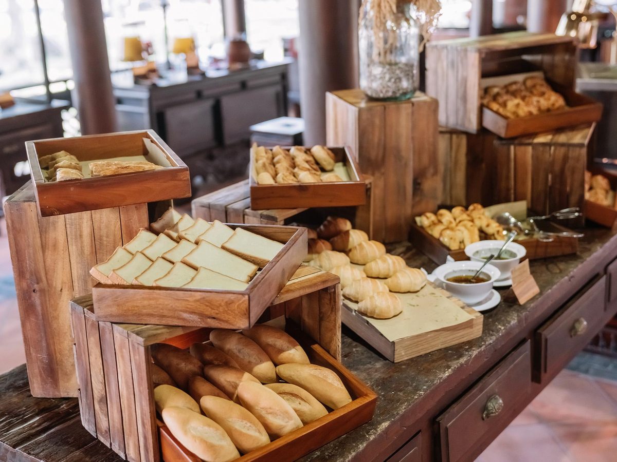 Wooden crates of fresh bread rolls and pastries on a buffet counter with warm light