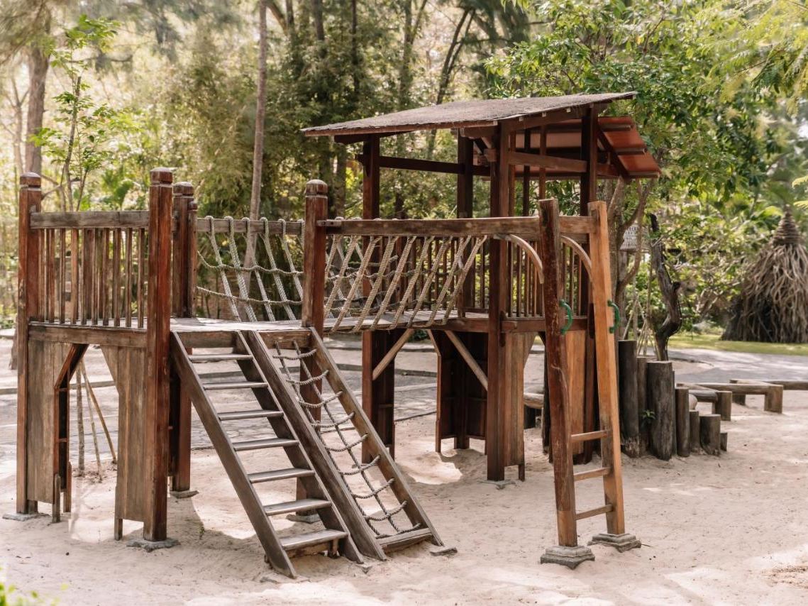 Sand playground with a wooden climbing frame, ladder and slide in the shade of casuarina trees
