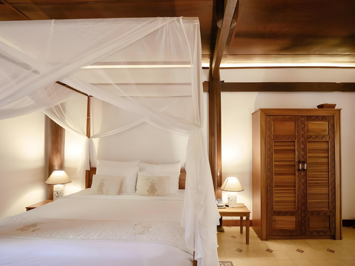 Bedroom with a four-poster bed under a white net, dark wood panelling and a tall wooden wardrobe