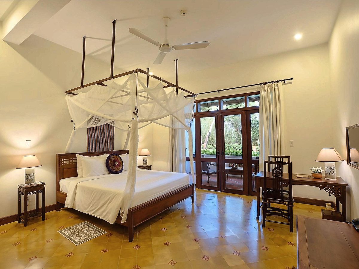 Bedroom with a four-poster bed under a white net, parquet floor, wooden desk and glass doors to a balcony